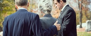 Woman being comforted by adult sons at a funeral 