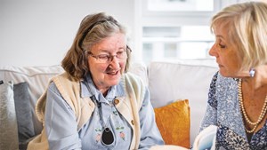 Two women chatting on sofa, elder woman is wearing a personal alarm pendant