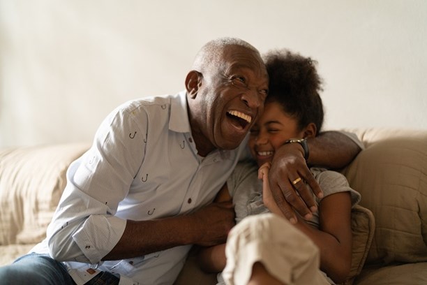 Laughing grandfather embracing granddaughter on a sofa