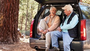 Couple seated in the open boot of hatchback putting on shoes for a walk