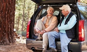 Couple seated in the open boot of hatchback putting on shoes for a walk