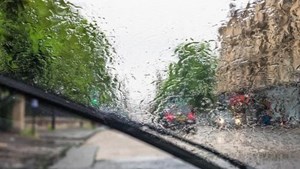 Blurry windscreen covered in raindrops being cleared by windscreen wipers