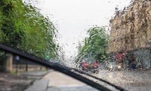 Blurry windscreen covered in raindrops being cleared by windscreen wipers