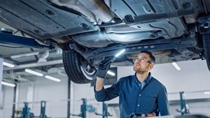 Mechanic with torch under the bonnet of an elevated car