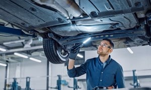 Mechanic with torch under the bonnet of an elevated car