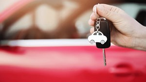 Car keys being held in front of red car