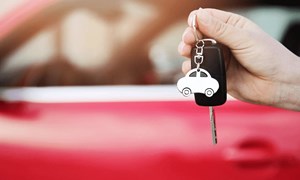 Car keys being held in front of red car