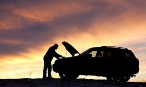 Broken down car with open bonnet and person looking at the engine during sunset