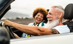 A older man and woman laughing and driving open top car