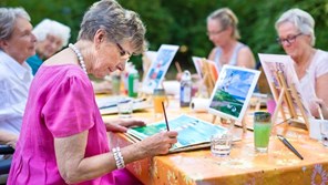 A group of older people do arts and crafts outside in a park.