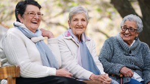 Three elderly women outside laughing on picnic bench together