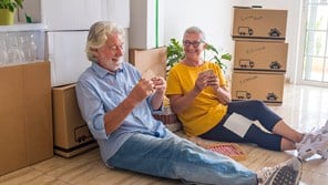 Couple take break while moving for a downsize, sitting on floor eating sandwiches.