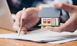 Person reviewing documents on a desk and holding a model house