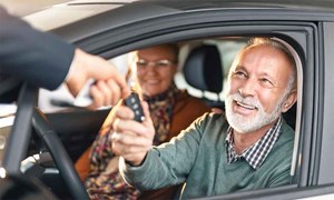 Couple in new car being handed the keys by a dealer