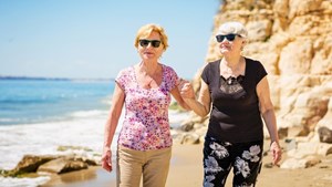 Older female couple walking together along a beach holding hands