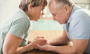 Anxious looking couple holding hands across a table