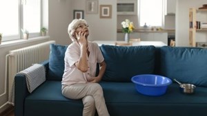 Woman sat talking on phone and looking up at ceiling with buckets on sofa