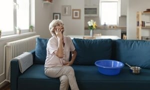 Woman sat talking on phone and looking up at ceiling with buckets on sofa