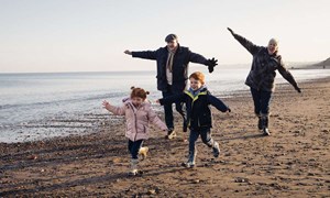 Grandparents and children running along beach