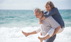 Older man giving a woman a piggyback on the beach