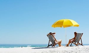 Couple sitting in deckchairs under a yellow parasol on a beach