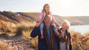 Older couple walking on a beach with grandchild on man's shoulders