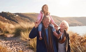 Older couple walking on a beach with grandchild on man's shoulders