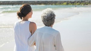 A mum and daughter walk along a sunny shoreline.